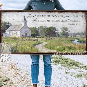 May include: A framed landscape art print featuring a church and a path leading to it, with the text "He makes me lie down in green pastures. He leads me beside quiet waters. Psalm 23:2." The artwork has a rustic, vintage style.
