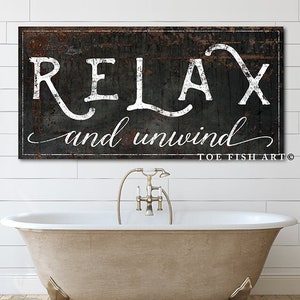 May include: Black and white sign with the text "Relax and unwind" in a distressed font. The sign has a rustic, weathered look and is hanging above a white clawfoot bathtub.