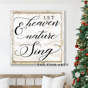 May include: A rustic wooden bench with two white pillows sits below a framed sign that reads "Let Heaven Nature Sing" in elegant black script. A decorated Christmas tree with red ornaments and lights stands to the right, with wrapped gifts at its base.