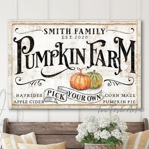 May include: A white sign with black text that reads "Smith Family Est. 2020 Pumpkin Farm". The sign also includes the text "Hayrides Apple Cider Pick Your Own Corn Maze Pumpkin Pie". The sign is hanging on a white wall above a wooden bench with two pillows and a potted plant.