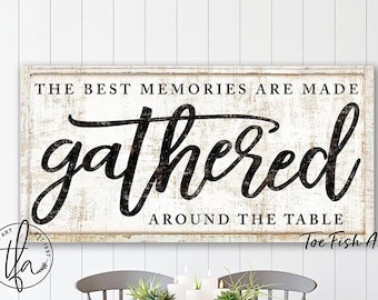 May include: A white wooden sign with black lettering that reads "The best memories are made gathered around the table." The sign is distressed and has a rustic look. The sign is hanging on a white wall above a wooden table with four chairs.