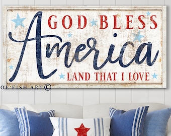May include: A white wooden sign with red and blue text that reads "God Bless America Land That I Love". The sign has a distressed look and is decorated with stars.