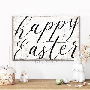 May include: White wooden sign with black script lettering that reads "happy easter". The sign is distressed and has a rustic look. The sign is hanging on a white wall.