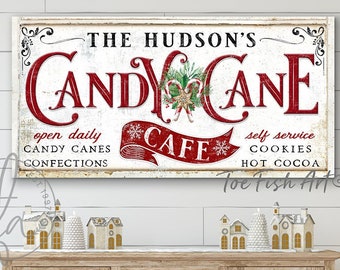 Puede incluir: Un letrero de pared rectangular con fondo blanco desgastado que presenta el texto THE HUDSON'S CANDY CANE CAFE en letras rojas y negras. El diseño incluye un gráfico central de bastón de caramelo, copos de nieve y texto sobre dulces, galletas y cacao.