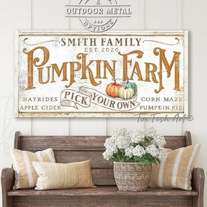 May include: A white sign with distressed lettering that reads "Smith Family Pumpkin Farm Est. 2020". The sign also includes the text "Hayrides Apple Cider Pick Your Own Corn Maze Pumpkin Pie" and a graphic of three pumpkins. The sign is hanging on a white wall above a wooden bench.