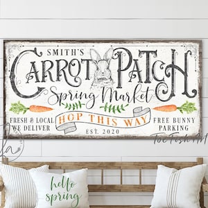 May include: A white wooden sign with black lettering that reads "Smith's Carrot Patch Spring Market" with a bunny rabbit illustration and the text "Fresh & Local, We Deliver, Hop This Way, Free Bunny Parking, Est. 2020".