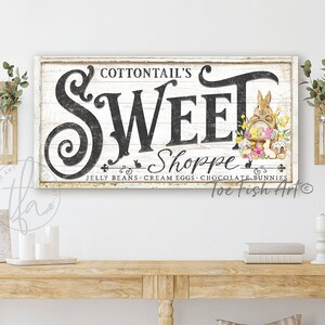 May include: A white wooden sign with black lettering that reads "COTTONTAIL'S SWEET Shoppe JELLY BEANS CREAM EGGS CHOCOLATE BUNNIES Toe Fish Art" with a watercolour illustration of a bunny holding a basket of Easter eggs.