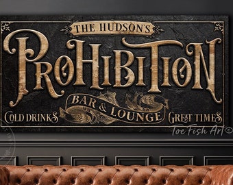 May include: A vintage-style sign with the text "The Hudson's Prohibition Bar & Lounge" in gold lettering on a black background. The sign also includes the text "Cold Drinks" and "Great Times" in smaller gold lettering. The sign is framed in a black frame and has a distressed look.