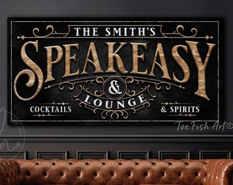 May include: A black framed sign with gold lettering that reads "The Smith's Speakeasy & Lounge Cocktails & Spirits". The sign is above a brown leather couch and a small black table. The sign has a vintage design.