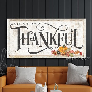 Peut inclure: Une pancarte en bois blanc vieillie avec le texte "So Very Thankful" en écriture cursive noire. La pancarte est décorée d'une petite citrouille, d'une pomme de pin, de glands et de feuilles d'automne.
