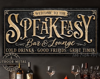 May include: A rectangular wall sign with a black textured background and gold lettering that reads WELCOME TO THE SPEAKEASY Bar & Lounge COLD DRINKS GOOD FRIENDS GREAT TIMES. The sign is positioned above a bar shelf with various glass bottles and stemware.