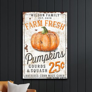 May include: A vintage-style sign with a white background and orange text that reads "WILSON FAMILY EST. 2020 FARM FRESH Pumpkins 25¢ GOURDS & SQUASH HAYRIDES CORN MAZE CIDER". The sign features a large orange pumpkin with a green stem.