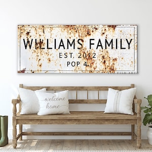 May include: A rustic metal sign with a white background and brown rust accents. The sign reads "Williams Family Est. 2012 Pop 4" in black lettering.