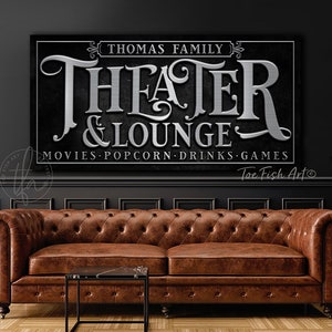 May include: Black and silver sign with the text "Thomas Family Theater & Lounge" and the words "Movies, Popcorn, Drinks, Games".
