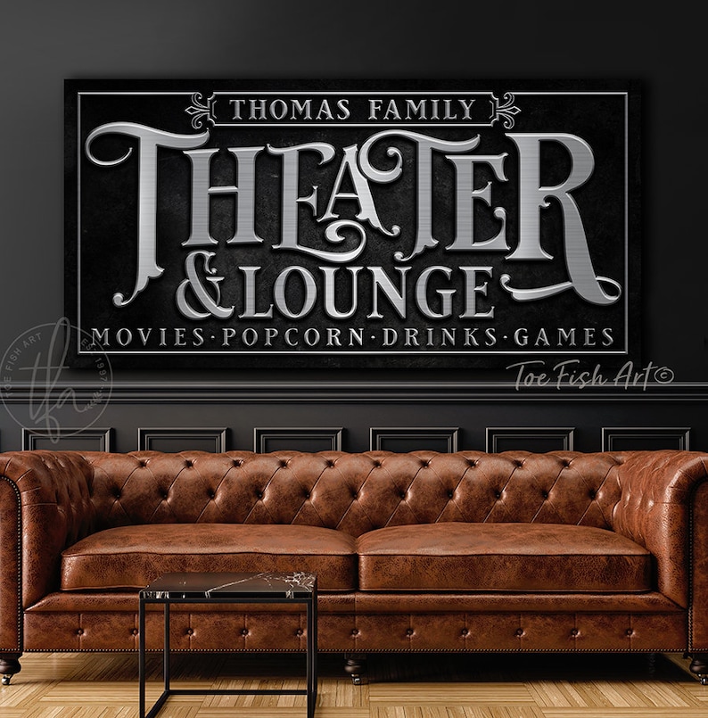 May include: Black and silver sign with the text "Thomas Family Theater & Lounge" and the words "Movies, Popcorn, Drinks, Games".