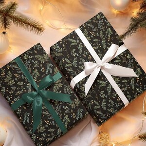 May include: Two wrapped gifts with black paper featuring a green and gold leaf pattern. One is tied with a white ribbon, the other with a green ribbon. The gifts are surrounded by Christmas decorations, including ornaments and pine branches.