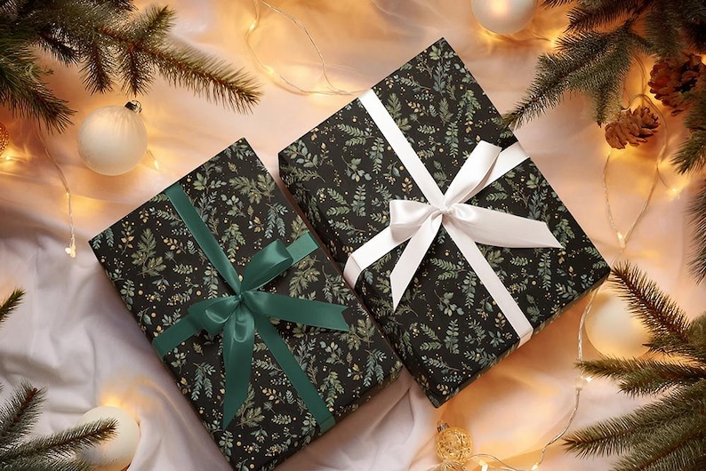 May include: Two wrapped gifts with black paper featuring a green and gold leaf pattern. One is tied with a white ribbon, the other with a green ribbon. The gifts are surrounded by Christmas decorations, including ornaments and pine branches.