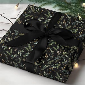 May include: A wrapped gift with black wrapping paper featuring a botanical pattern of green and gold leaves on a black background. A wide black satin ribbon is tied in a bow around the gift.