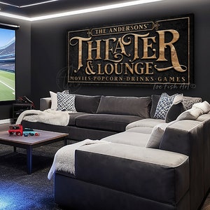 May include: A black and gold sign with the text "The Andersons' Theater & Lounge" and the words "Movies, Popcorn, Drinks, Games" below. The sign is hanging on a black wall in a home theater room.