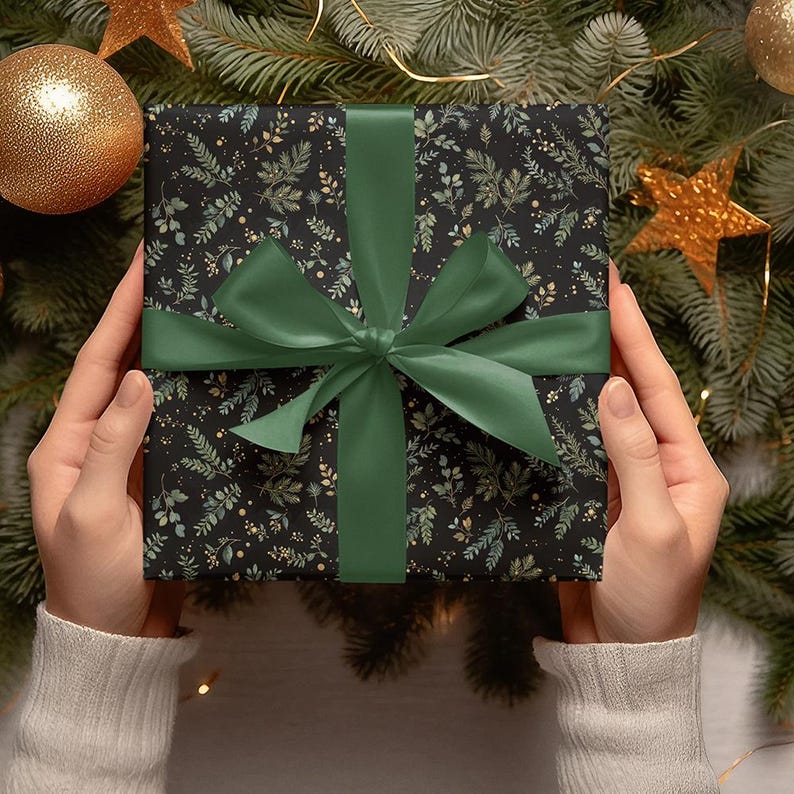 May include: A wrapped gift with a black background and a botanical pattern of green and gold leaves. The gift is tied with a dark green satin ribbon and bow. The gift is surrounded by Christmas decorations.