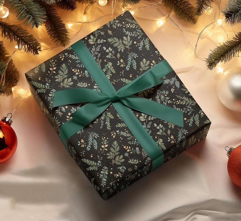 May include: A wrapped gift box with a dark background and a pattern of green and gold leaves. The box is tied with a wide, emerald green satin ribbon and bow. Christmas ornaments and evergreen branches are in the background.