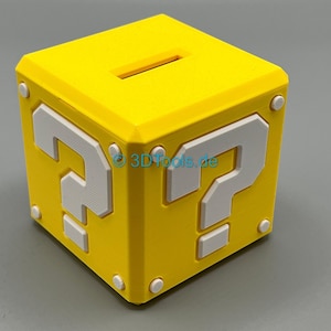 Könnte beinhalten: Eine gelbe, würfelförmige Spardose mit weißen Fragezeichen und Akzenten, die an ein klassisches Videospiel erinnert. Die Oberseite hat einen Schlitz zum Einwerfen von Münzen. Das Design ist ein 3D-gedrucktes Objekt.