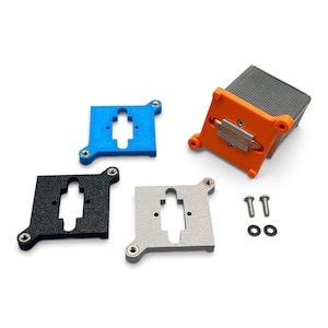 Peut inclure: Un composant de refroidissement informatique avec un cadre orange et des ailettes métalliques, accompagné de trois supports de montage carrés en bleu, noir et argent. Chaque support présente une découpe centrale et des trous de vis aux coins.