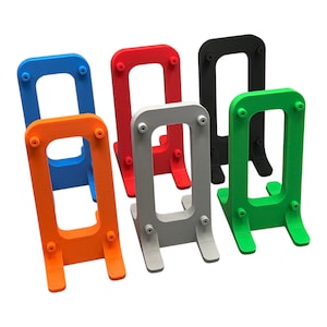 May include: A collection of six upright display stands in blue, orange, red, gray, black, and green. Each stand features a rectangular frame with four small circular protrusions on the front face and two sturdy feet extending from the base.