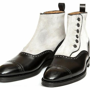 Puede incluir: Botines de cuero bicolor. Los zapatos tienen puntera y talón negros, con la parte superior de ante gris claro. Una bota tiene cierre de botones, la otra con cremallera. Ambas tienen una lengüeta en la parte trasera.