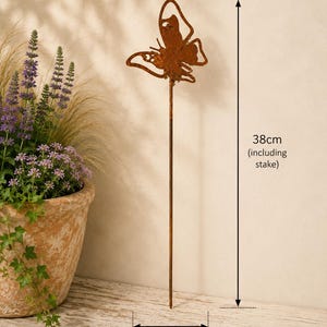 May include: A rust-colored metal butterfly garden stake with a cutout wing design. The total height of the stake is 38 cm, and the width of the butterfly is 9 cm. The metal has a weathered, oxidized finish, and the stake is thin and straight.