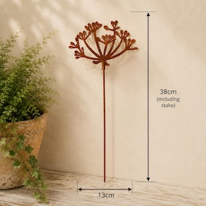 May include: A rust-colored metal garden stake featuring a stylized floral or seed head design with multiple branching stems. The total height of the stake is 38 cm, and the width of the decorative top section is 13 cm, as indicated by labels.