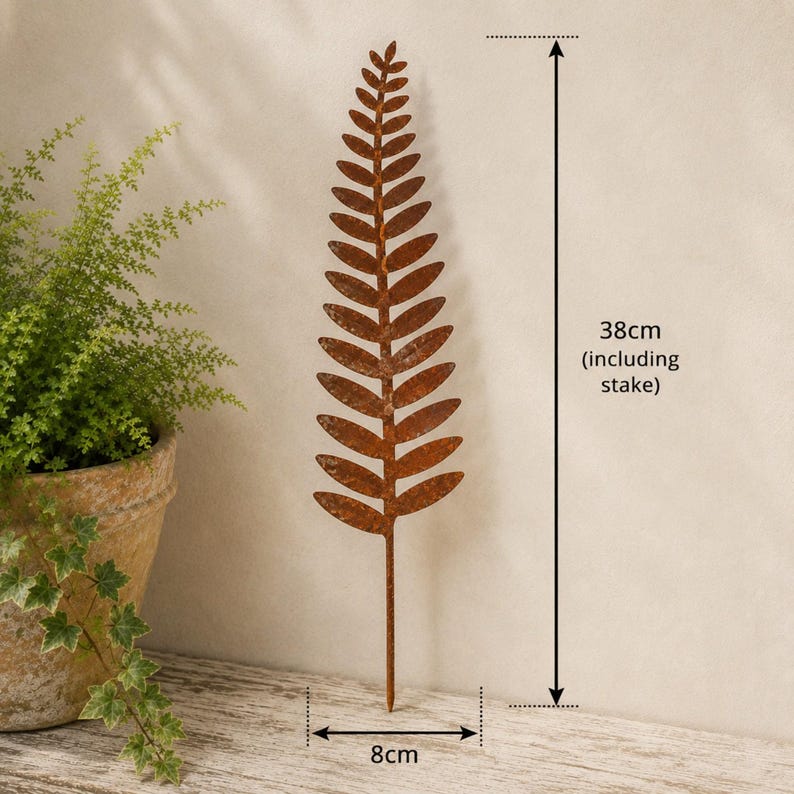 May include: A rust-colored metal fern leaf garden stake with a textured finish. The decorative plant ornament features a pointed tip and symmetrical leaves along a central stem. It measures 38 cm in total height and 8 cm in width as indicated.
