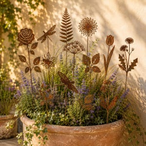 May include: A collection of rust-colored metal garden stakes featuring silhouettes of a rose, a dragonfly, a bee, a fern leaf, a dandelion, a tulip, and other wildflowers. Each decorative stake is mounted on a thin metal rod for display.