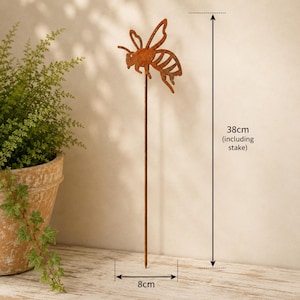 May include: A rust-colored metal bee garden stake featuring a cutout bee silhouette attached to a thin vertical rod. The total height of the garden ornament is 38 cm, and the width of the bee figure is 8 cm, as indicated by the measurement labels.