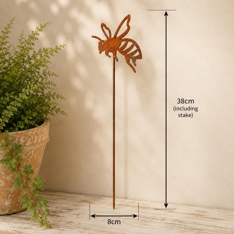 May include: A rust-colored metal bee garden stake featuring a cutout bee silhouette attached to a thin vertical rod. The total height of the garden ornament is 38 cm, and the width of the bee figure is 8 cm, as indicated by the measurement labels.