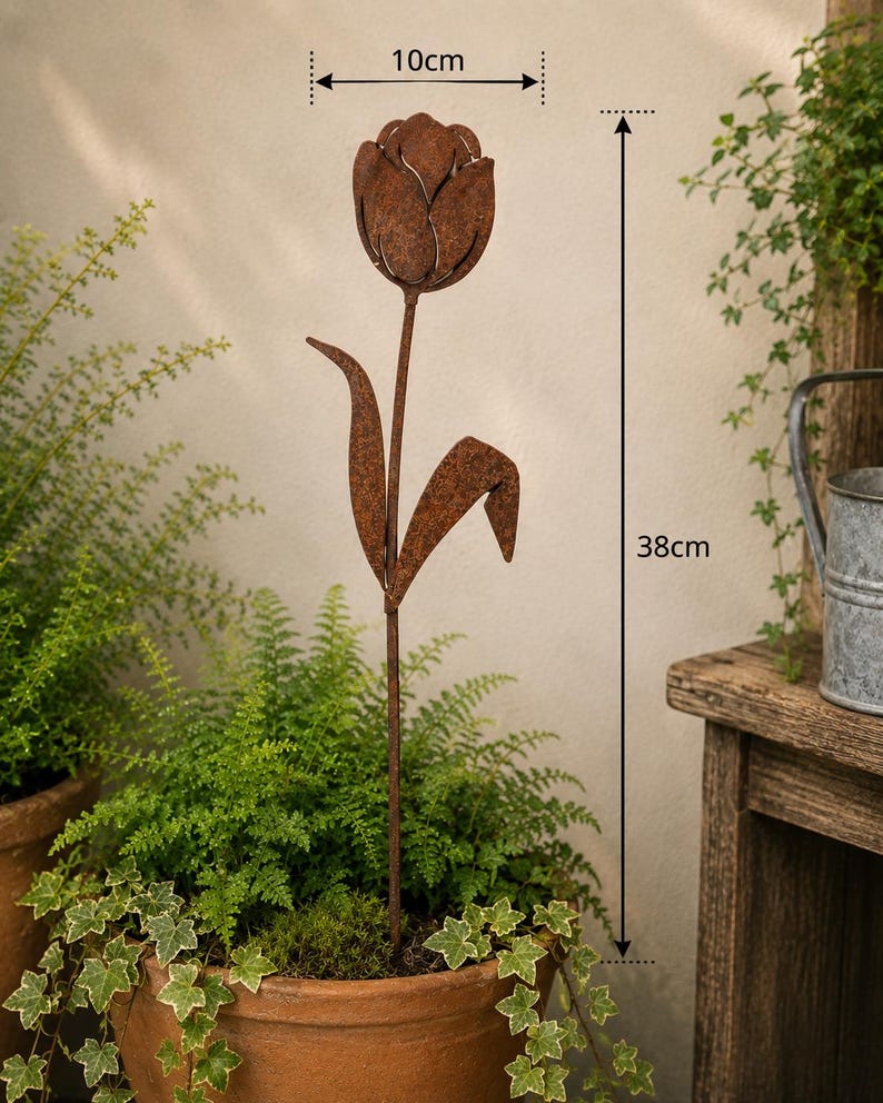 May include: A rust-colored metal tulip garden stake featuring a flower head and two leaves on a thin stem. The flower head measures 10 cm in width, and the total height of the garden stake is 38 cm. The metal surface has a textured, weathered finish.
