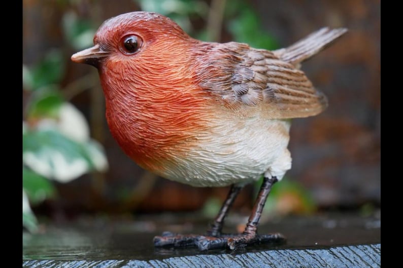 May include: A detailed figurine of a European robin. The bird has a red-orange breast, a brown back, and a white belly. Its small, dark legs are visible, and it is perched on a surface. The figurine is a decorative item.