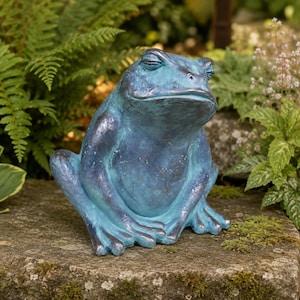May include: A decorative frog figurine featuring a weathered blue and teal patina finish. The frog is depicted in a seated, resting position with its eyes closed, showcasing a smooth, rounded body shape and detailed webbed feet resting on the surface.