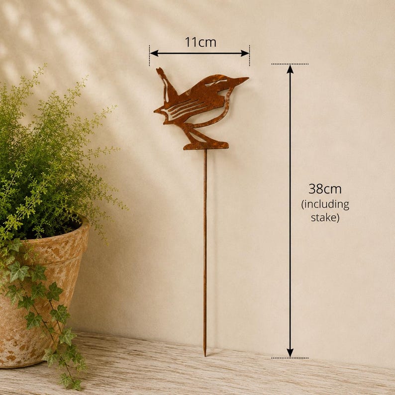 May include: A rust-colored metal bird garden stake featuring a cutout silhouette design. The bird figure measures 11 cm in width, and the total height of the garden stake, including the thin metal rod, is 38 cm as indicated by the labels.