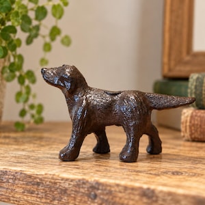 May include: A dark brown, textured cast iron figurine of a standing dog. The sculpture features a detailed, rugged surface finish, capturing the canine in a side profile stance with its head slightly lifted and tail extended horizontally.