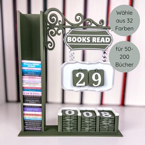 May include: A dark green "Books Read" sign with a built-in book holder and a counter. The sign has a decorative scroll design and a white and green counter showing "29". The book holder contains miniature book spines. The text "W&auml;hle aus 32 Farben" and "f&uuml;r 50-200 B&uuml;cher" are also visible.