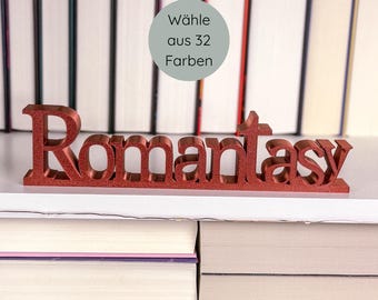 May include: A red glittery "Romantasy" word sign displayed on a white shelf, with a backdrop of stacked books. A circular graphic in the background reads "Wähle aus 32 Farben". The sign is a decorative item for book lovers.