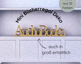 May include: A gold-colored "AudioBooks" decorative sign on a white shelf. The sign is in a cursive font. Text above the sign reads "Mini Bücherregal Deko". A circular graphic states "Wähle aus 32 Farben".