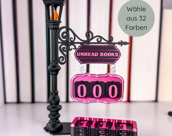 May include: A black and pink Unread Books sign with a street lamp design. The sign has a counter showing "000" and a separate counter showing "111". The lamp has an orange light. The sign reads "Unread Books".