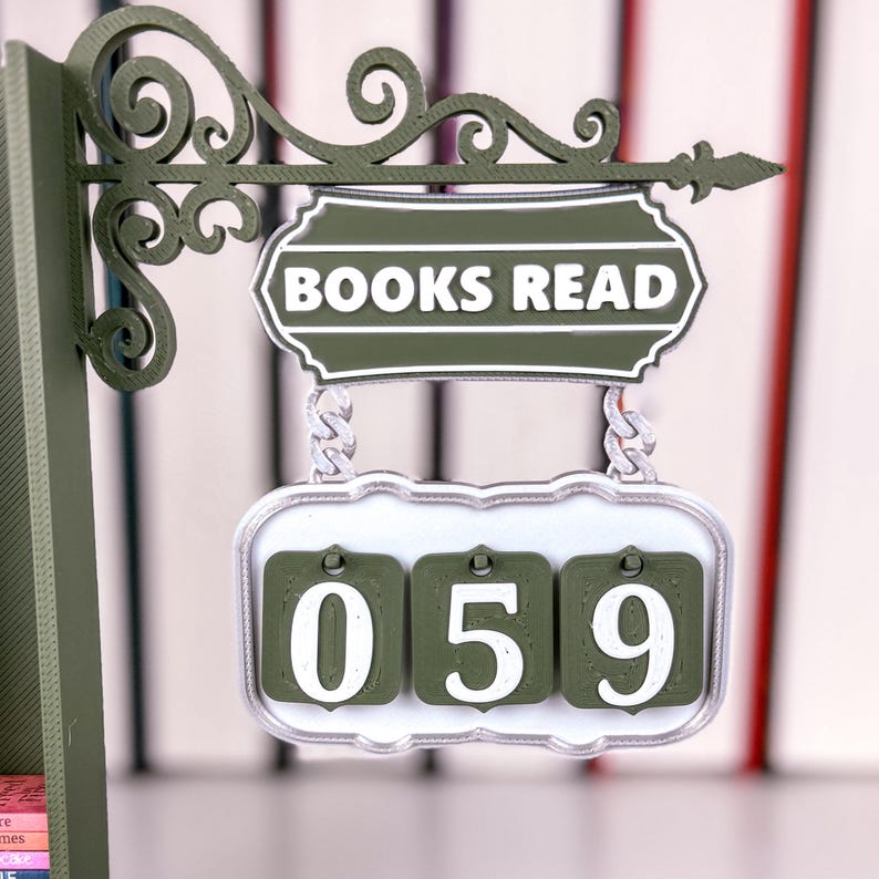 May include: A green and white "BOOKS READ" sign with a counter showing "059". The sign features an ornate, scrollwork bracket. The counter is designed to track the number of books read.