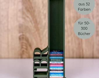 May include: A dark green wooden bookshelf shaped like the letters "IBR" holding a stack of books. The text "Wähle aus 32 Farben" and "für 50-300 Bücher" are in the background. The books have colorful spines.