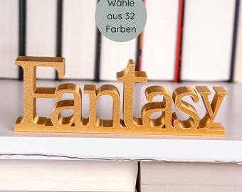 May include: A gold-colored "Fantasy" word sign, displayed on a shelf with a stack of books in the foreground and more books in the background. A circular graphic in the upper right corner reads "Wähle aus 32 Farben".