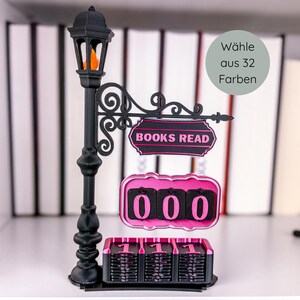 Könnte beinhalten: Eine schwarze dekorative Straßenlaterne mit einem Schild mit der Aufschrift "BOOKS READ" und einem Zähler, der "000" anzeigt. Die Lampe hat eine orangefarbene Flamme und einen rosa-schwarzen Zähler. Das Schild sagt "Wähle aus 32 Farben".