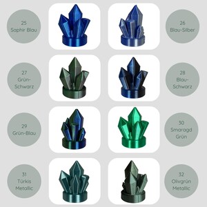 May include: A collection of crystal-shaped sculptures in various colors, including blue, green, and teal. Each sculpture is displayed on a white background. The image includes text labels with color names such as "Saphir Blau" and "Smaragd Gr&uuml;n".