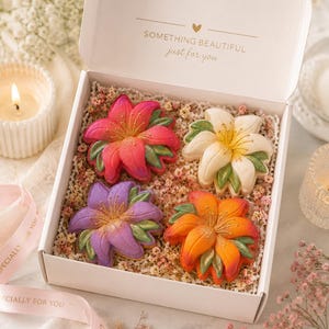 May include: A white gift box containing four flower-shaped cookies nestled in dried flowers. The cookies are colored pink, white, purple, and orange with green leaf accents. The box lid features the text SOMETHING BEAUTIFUL just for you.